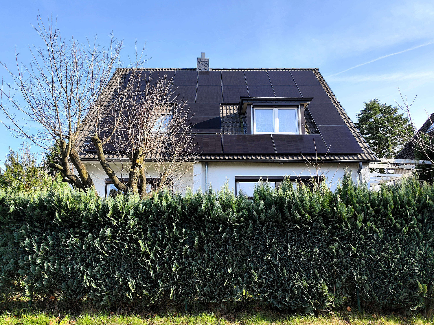 Haus hinter Hecke, auf dem Dach Solarpanels