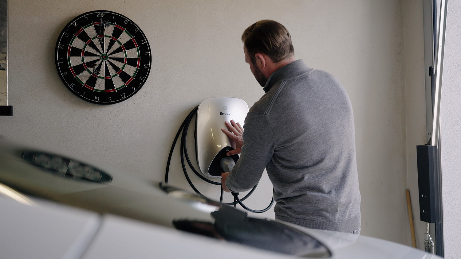 Garage Mann greift nach Stecker einer Wallbox, um sein E-Auto im Vordergrund zu laden